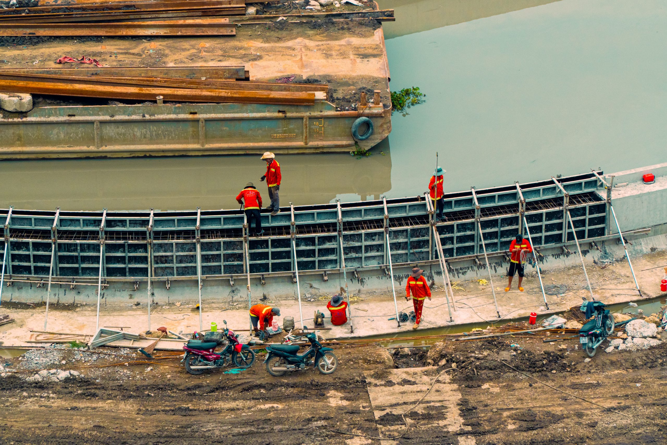 Aerial view of construction workers building canal infrastructure with visible equipment and waterway.